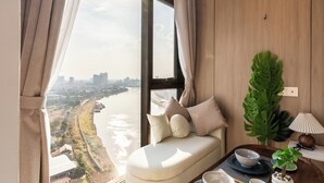 A room with a view of a river, a sofa with cushions, a table with a bowl and chopsticks, and a plant. - Vue Aston Condominium by Soben Homes (Phnom Penh)