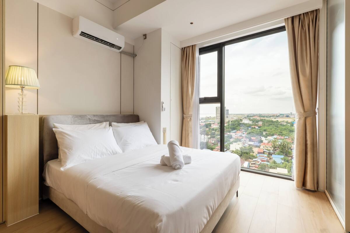 Ein Hotelzimmer mit einem großen Bett, Blick auf die Stadt und einer Klimaanlage.