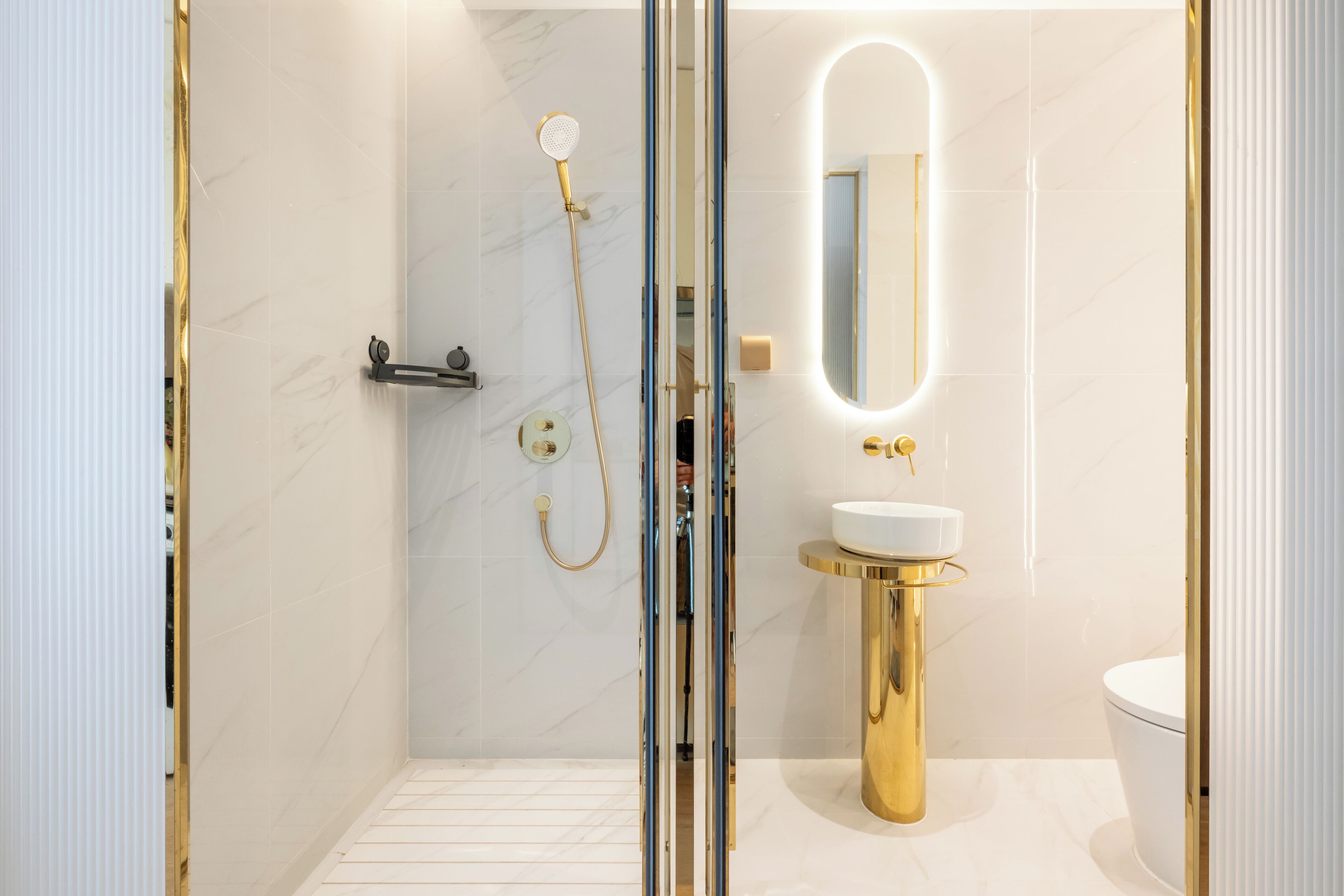 A modern bathroom with a glass-enclosed shower, a gold pedestal sink, and a large mirror.