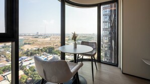 A corner room with a large window, a round table, two chairs, and a vase with flowers. - Vue Aston Condominium by Soben Homes (Phnom Penh)