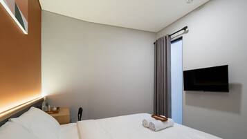 A hotel room with a bed, a bedside table, a TV mounted on the wall, and a window with curtains.