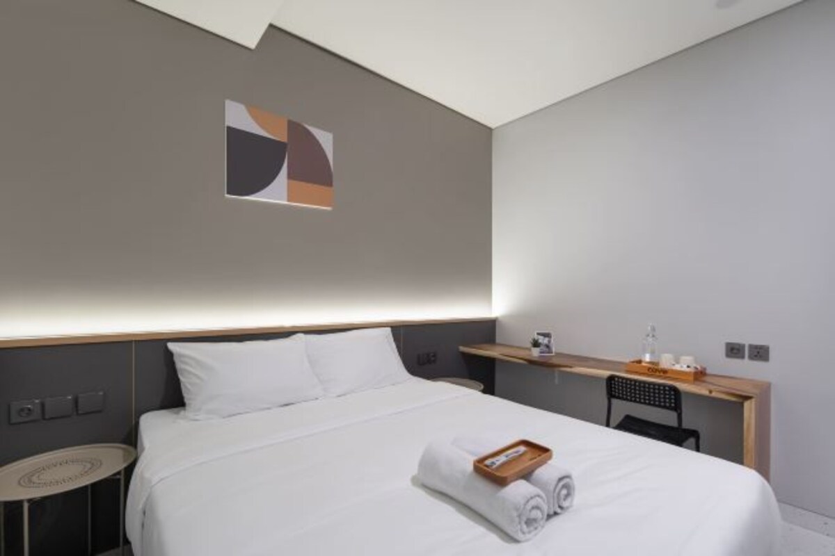A modern hotel room with a neatly made bed, a small desk, and a wall-mounted shelf.