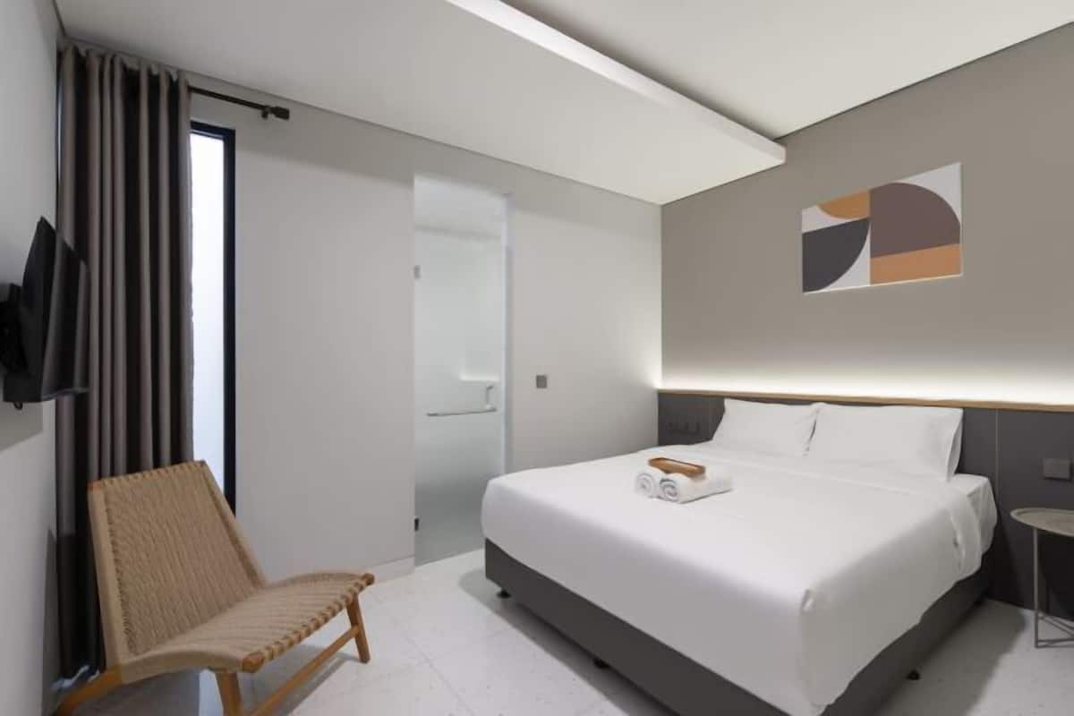 A hotel room with a bed, a chair, a TV, and a wall-mounted artwork.
