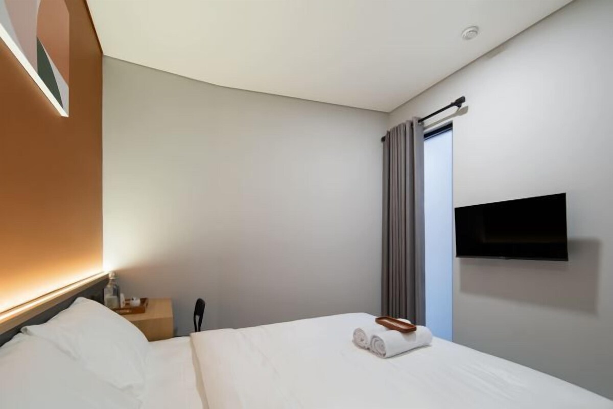 A hotel room with a bed, a nightstand, a TV mounted on the wall, and a window with curtains.