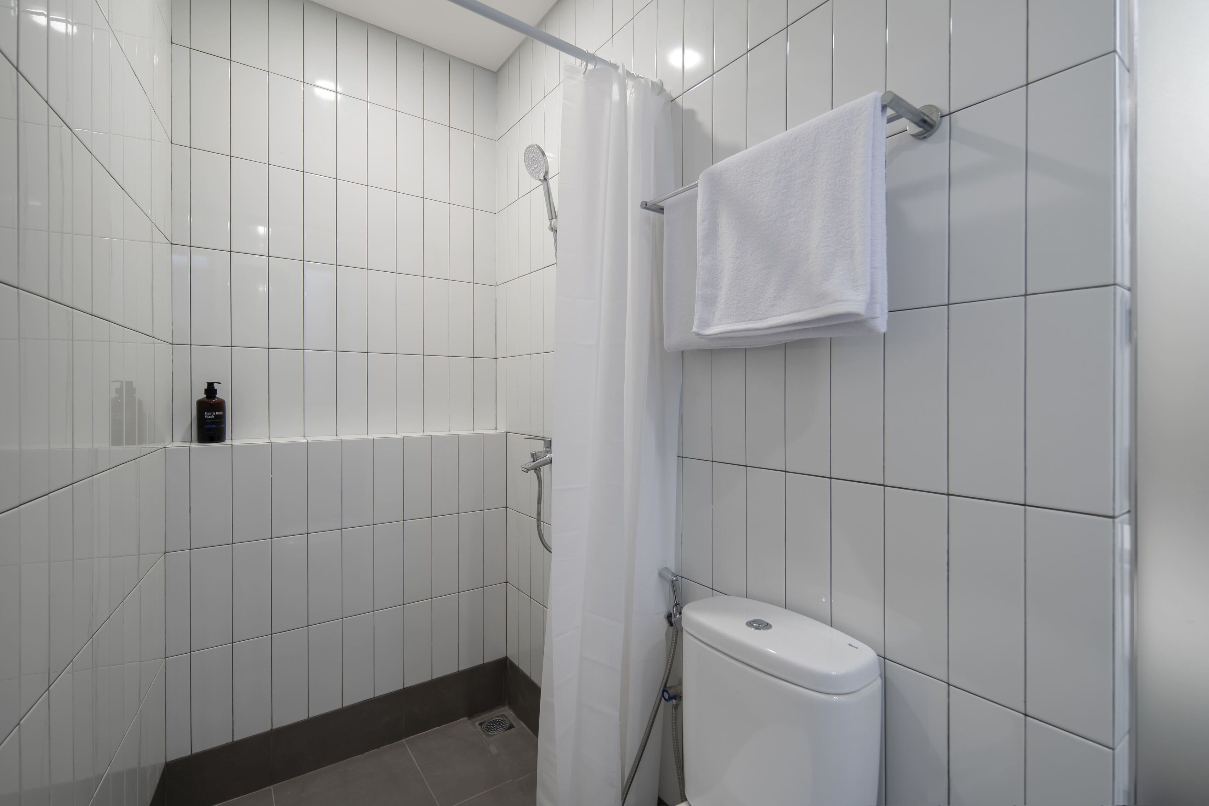 Een badkamer met witte tegels, een douche, een toilet en een handdoekhouder.