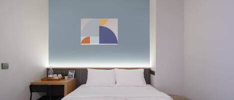 A hotel room with a bed, a desk, a chair, a nightstand, a wall art piece, and a tray with towels.