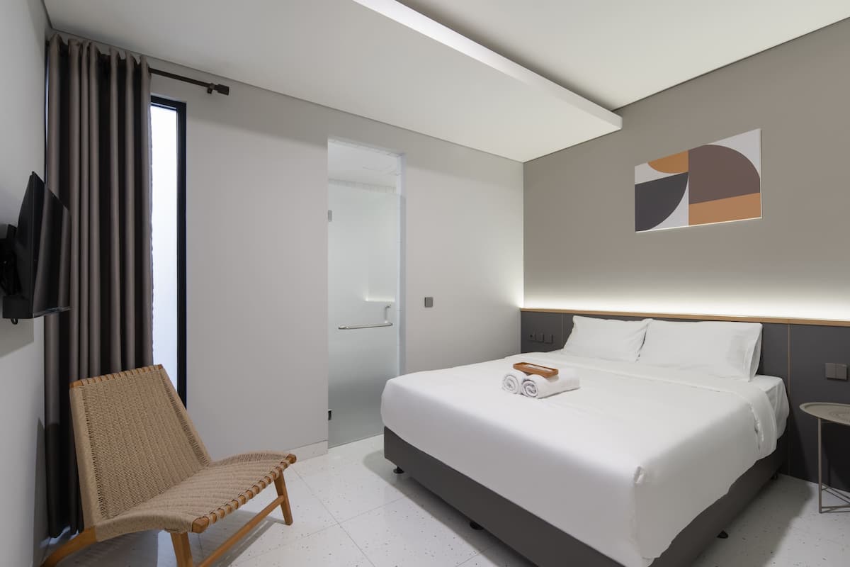 A hotel room with a bed, a chair, a wall-mounted TV, and a door.