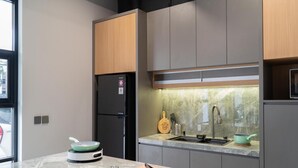 A modern kitchen with a black refrigerator, a wooden cutting board, and a green pot on the counter. - Cove Vaia (Bandung)