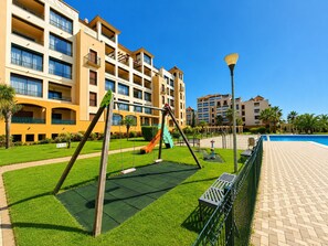 A playground with swings and a slide, surrounded by a well-maintained lawn and a pool area.