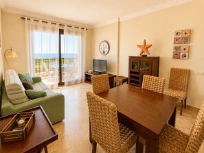 A living room with a green sofa, a wooden dining table, wicker chairs, a television, and a starfish decoration. - Los Pelicanos, 2 bedrooms with sea views - Ref.418 (Punta del Moral)