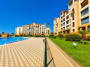 A hotel with a swimming pool, a paved walkway, and a well-maintained lawn.