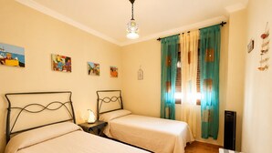 Une chambre avec deux lits, une petite table, une lampe, un radiateur et une fenêtre avec des rideaux.