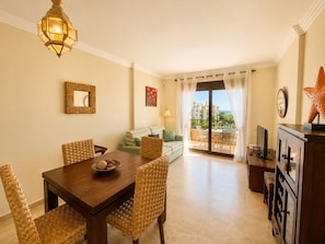 A dining area with a wooden table and wicker chairs, a sofa, and a balcony with a view.