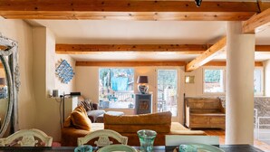 Ein gemütliches Wohnzimmer mit Holzbalken, einer Couch, einem Couchtisch mit Gläsern und Blick auf einen Balkon mit Gartenmöbeln.