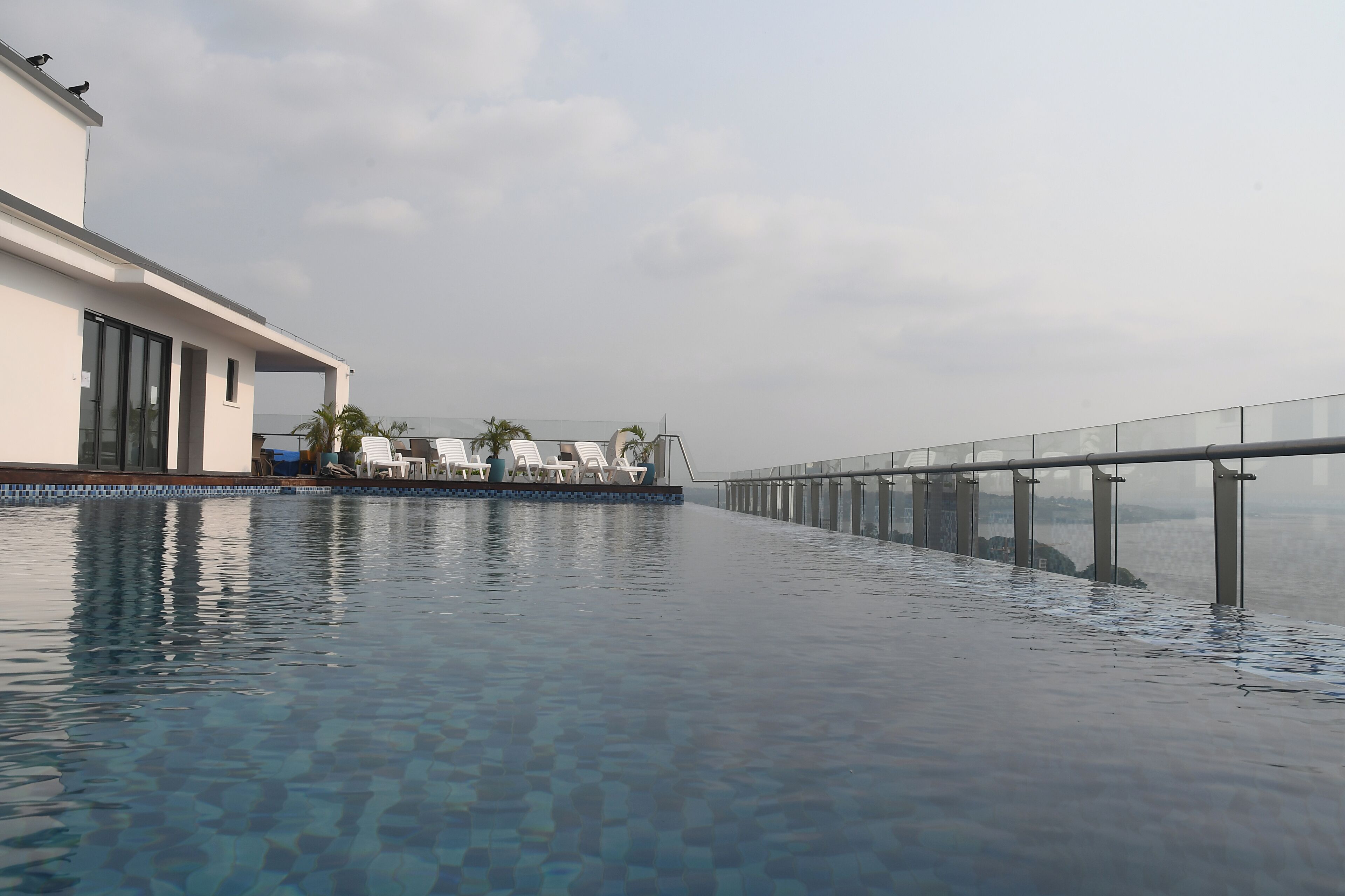 Une piscine à débordement dotée de chaises longues et d’une balustrade en verre donnant sur une étendue d’eau.