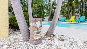 Area piscina con lettini, una scultura a forma di testa tiki e palme.