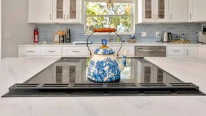 Una cucina moderna con mobili bianchi, un'isola con piano in vetro e una teiera a fiori blu.