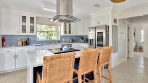 Una cucina moderna con mobili bianchi, un'isola centrale, sedie in vimini e una ventola a soffitto.