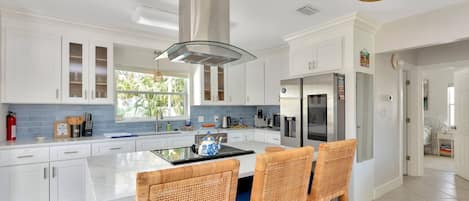 A modern kitchen with white cabinetry, a central island, wicker chairs, and a ceiling fan.