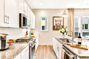 A modern kitchen with white cabinets, a granite countertop, a stainless steel sink, and a dining area with a vase of flowers.