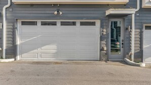 Een woonhuis met twee verdiepingen, een garage, een klein portaaltje en een raam met uitzicht op de straat.