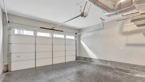 Een garage met een witte deur, een projector aan het plafond en een betegelde vloer.