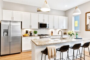 A modern kitchen with white cabinets, stainless steel appliances, a granite countertop, and bar stools.