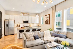 A modern kitchen with white cabinets, a stainless steel refrigerator, and a central island with bar stools. - Summer rooftop deck, 2-car garage, chef's kitchen near Broadway (Nashville)
