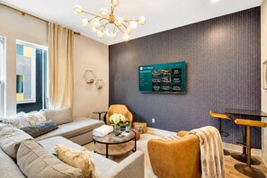 A modern living room with a sofa, armchair, coffee table, and a wall-mounted TV displaying a menu.