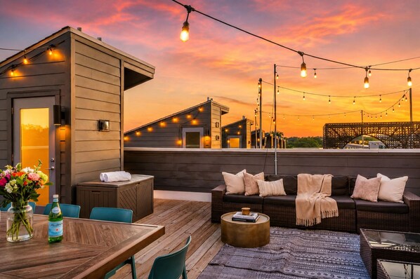 An outdoor patio with a wooden table, chairs, a sofa, and string lights against a sunset backdrop. - Fall Nashville escape | sleeps 12 | 4BR townhome near Nissan Stadium (Nashville)