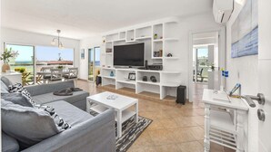 A modern living room with a grey sofa, a flat-screen TV, and a white entertainment unit.