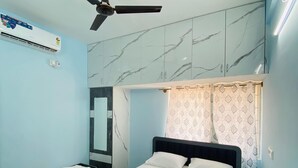 A bedroom with a bed, a ceiling fan, a wall-mounted air conditioner, and a bathroom with a mirror and sink. - Jc Residence (Bangaluru)