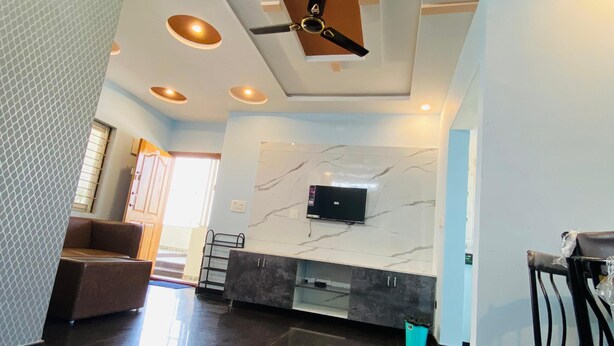 A spacious living area with a ceiling fan, recessed lighting, a marble backsplash, and a flat-screen TV mounted on the wall. - Jc Residence (Bangaluru)