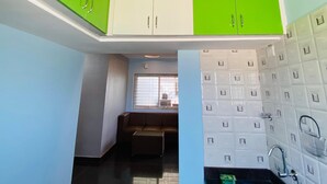 A modern kitchen with green and white cabinets, a built-in sink, and a window with blinds. - Jc Residence (Bangaluru)