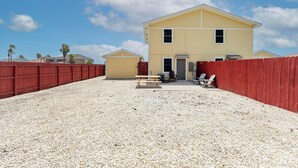 A two-story yellow building with a red fence, a gravel driveway, and a picnic table. - The Island Gem: Coastal Getaway (Corpus Christi)