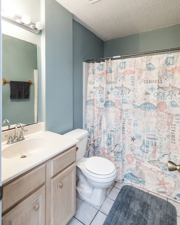 A bathroom with a white sink, a toilet, and a shower curtain with nautical designs.