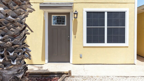 A yellow building with a gray door and a window. - The Island Gem: Coastal Getaway (Corpus Christi)