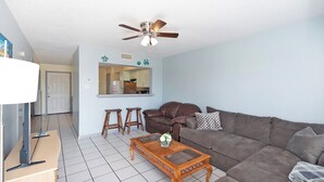 A living room with a brown leather sofa, a wooden coffee table, and a ceiling fan. - The Island Gem: Coastal Getaway (Corpus Christi)