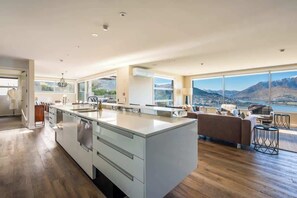 A modern kitchen with a large island, a dining area with a sofa and chairs, and a view of mountains through large windows.