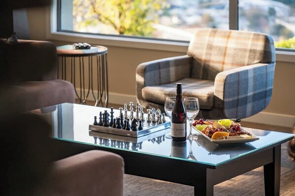 A glass-top table with a chessboard, a bottle of wine, and a fruit platter.