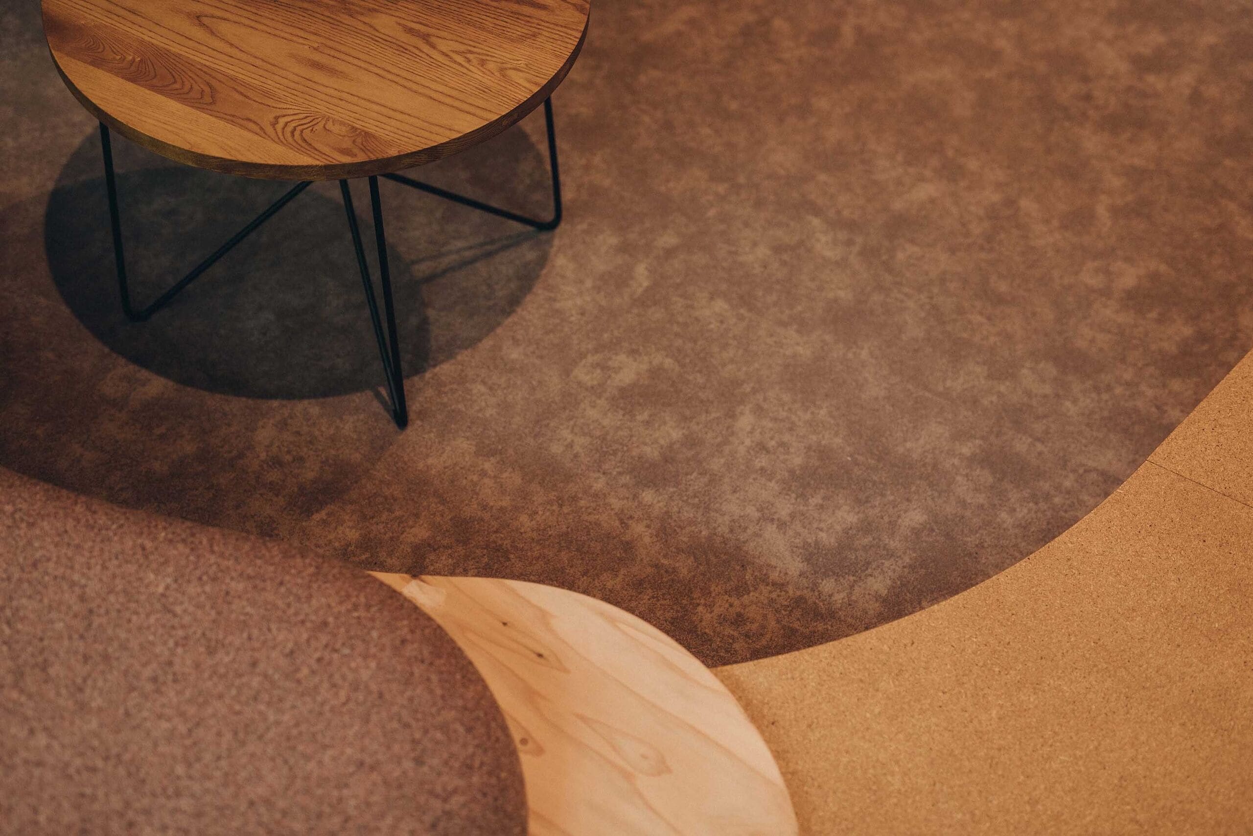 A round wooden table with metal legs on a textured floor.