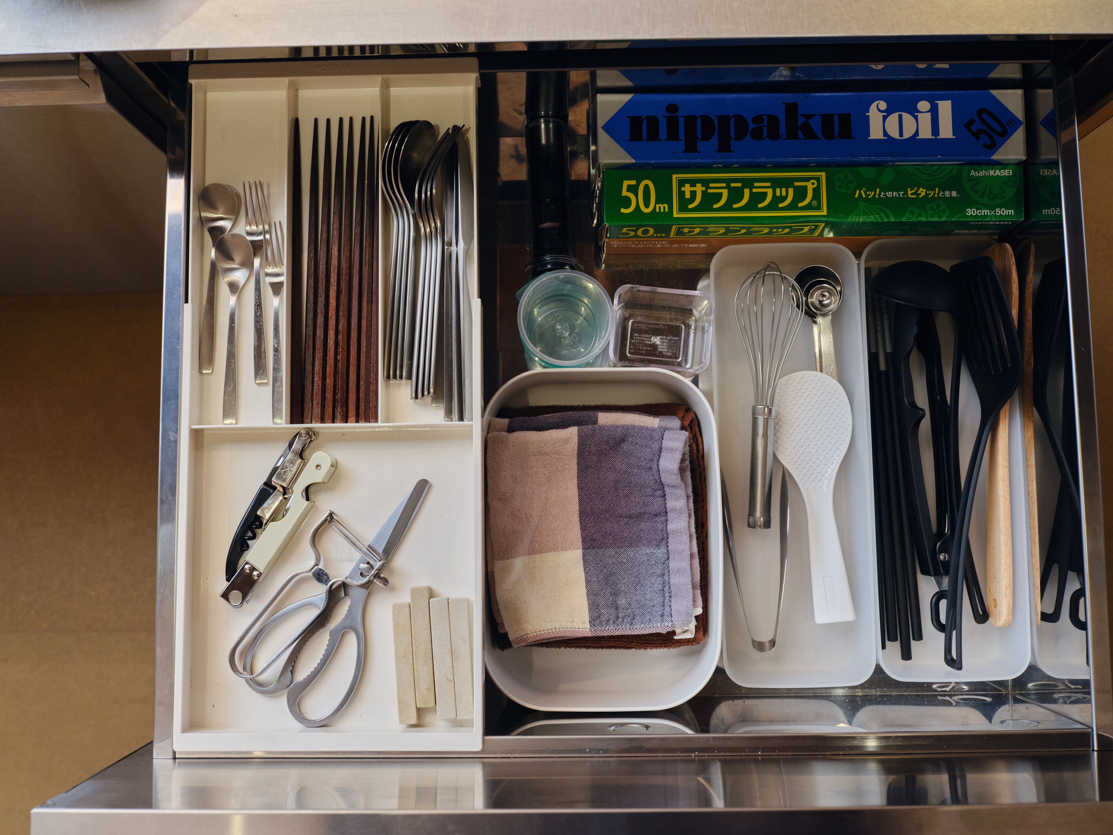 A kitchen drawer with utensils, a whisk, a spatula, and a package of nippaku foil.