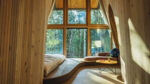 A bedroom with a curved bed, a small round table, and a window overlooking a forest. - SANU 2nd Home Karuizawa 1st (Karuizawa)