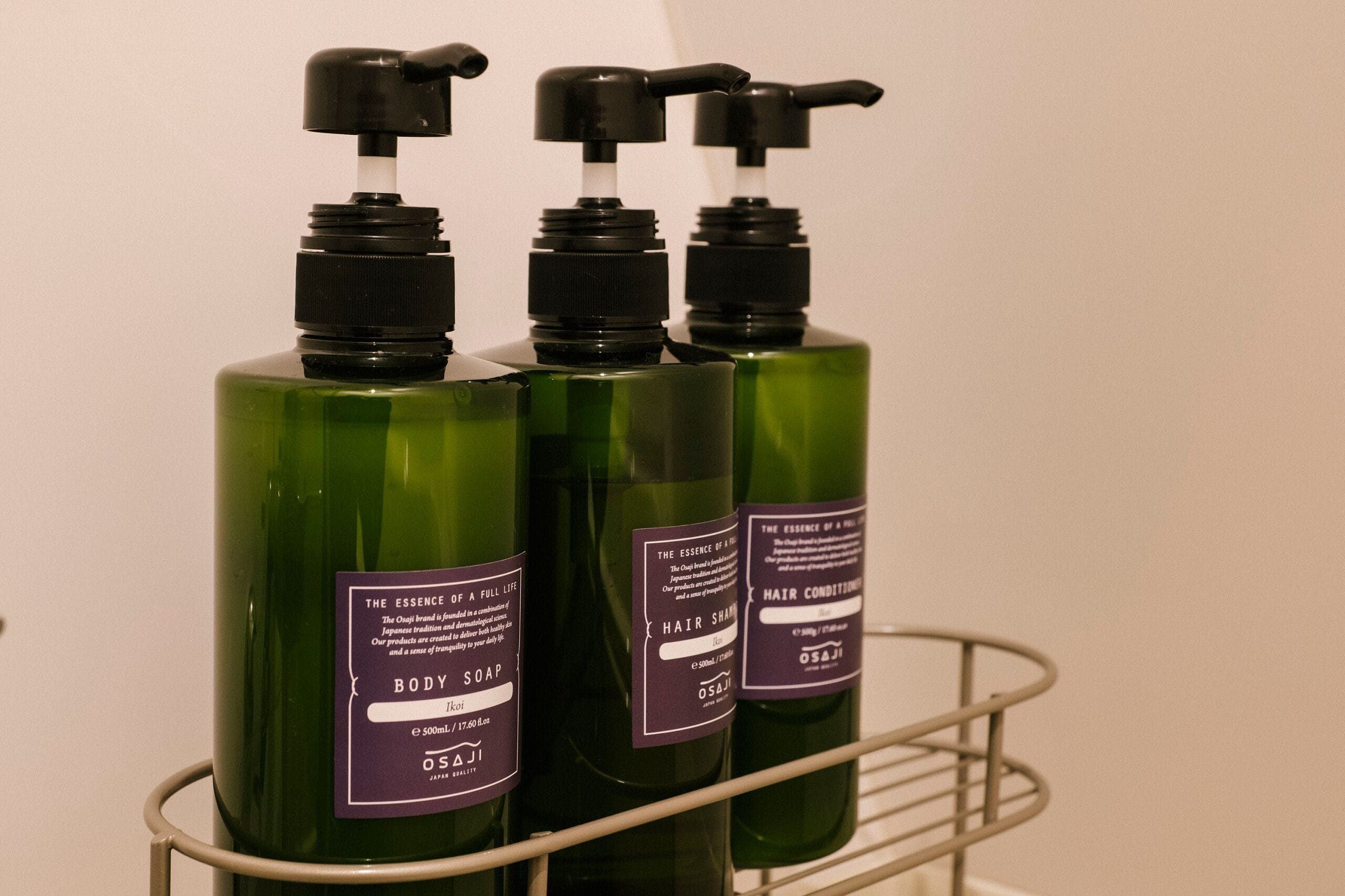 Three bottles of body soap and hair conditioner on a metal shelf.