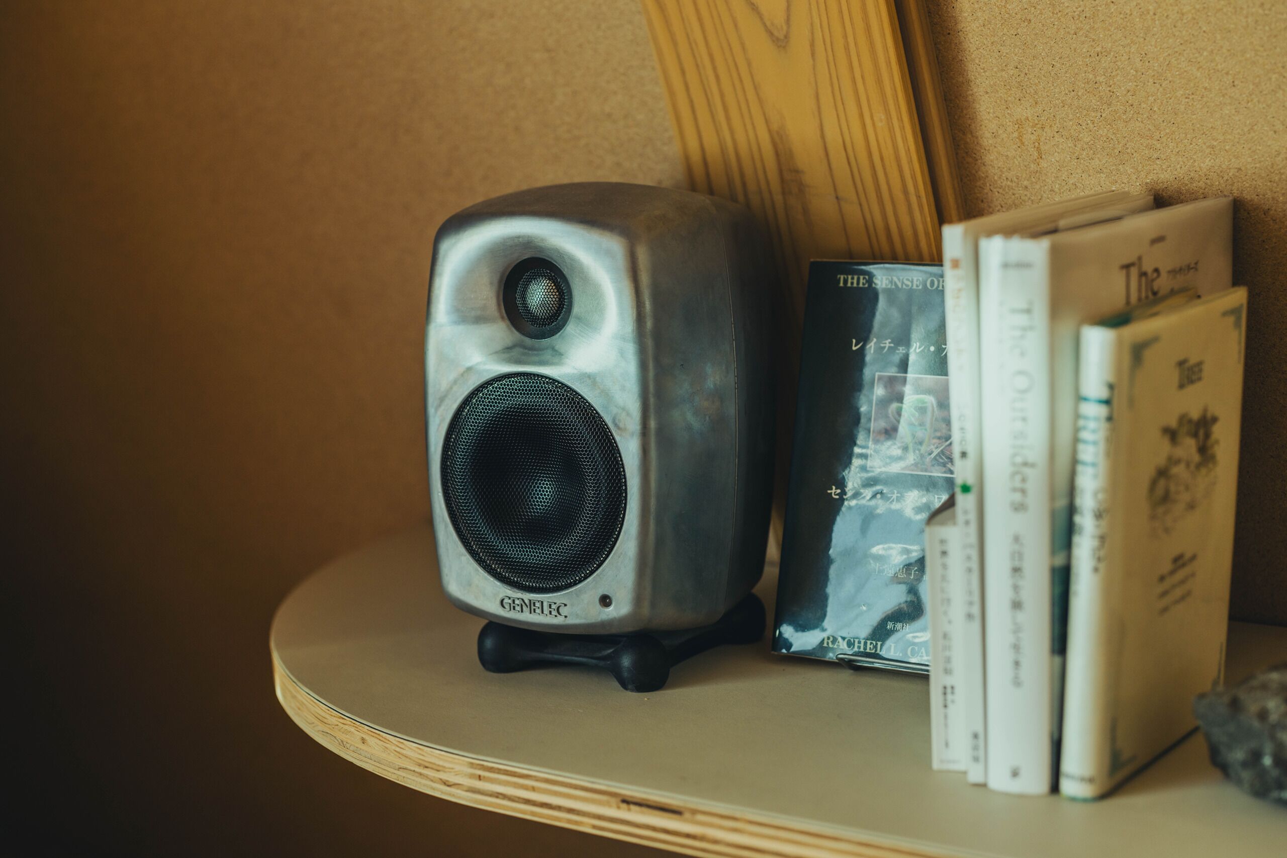 A Genlec speaker on a wooden shelf with books.