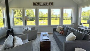Ein gemütliches Wohnzimmer mit hohen Decken, einem großen Fenster mit Blick auf Grünflächen und einem Schild mit der Aufschrift 'WANNAPONDA'.