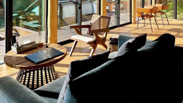 Un interior moderno con amplios ventanales, techo de madera y una zona de estar acogedora con sofá y sillones.