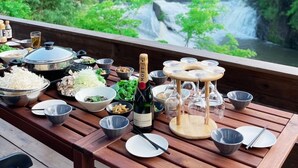 Una mesa de madera dispuesta con diversos platos, una botella de champán Moët Chandon, y vista a una cascada y un bosque.