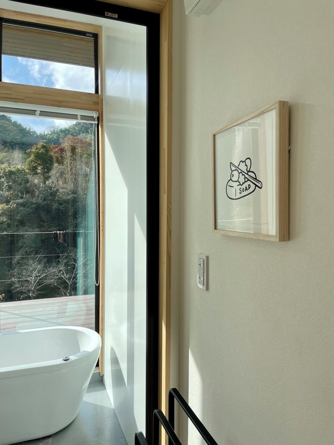 Une salle de bain moderne avec une grande baignoire, une fenêtre donnant sur une forêt et un tableau encadré au mur.