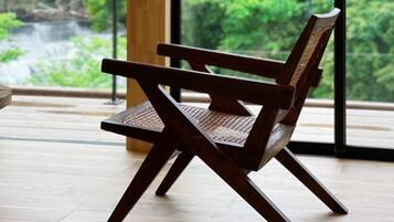 A wooden chair with a woven seat and backrest, positioned in a room with large windows overlooking a lush green forest and a waterfall.